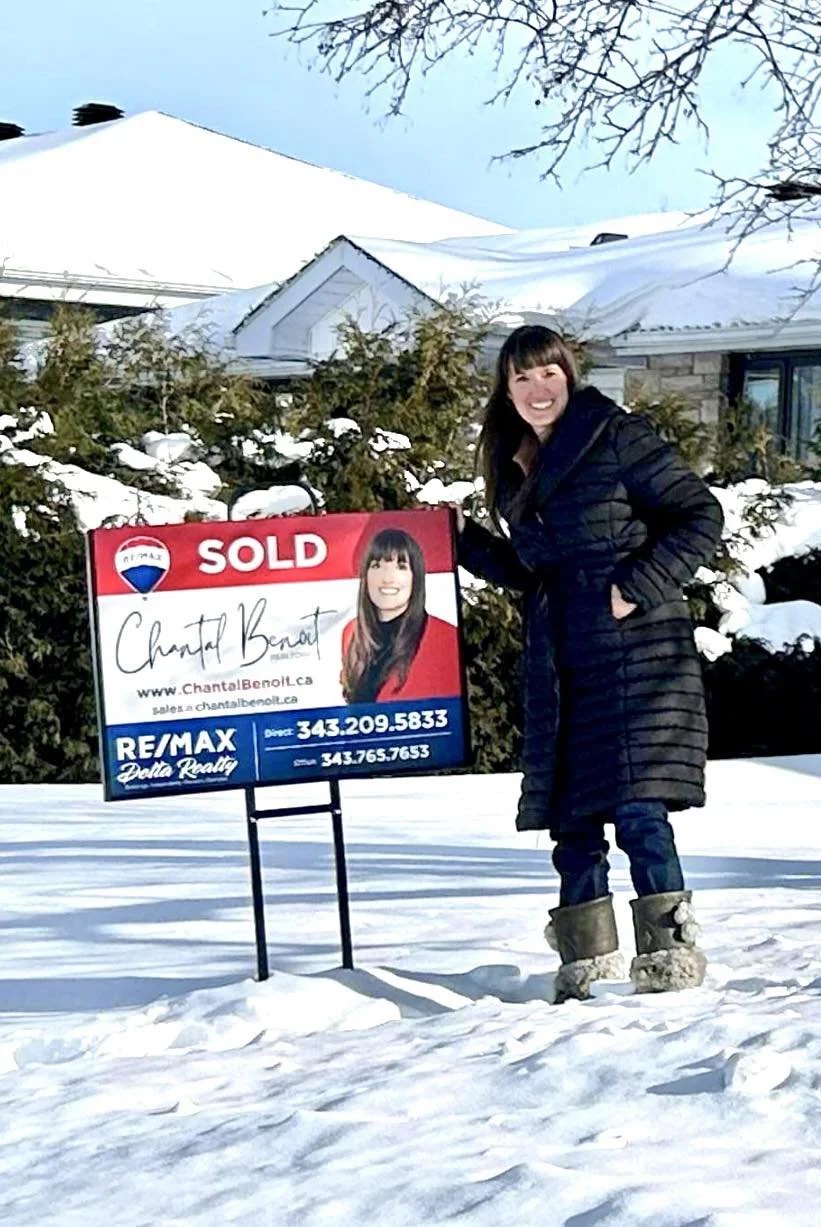 Chantal Benoit holding a Sold sign in front of a home in the snow